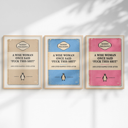 Three framed vintage-style book covers titled 'A Wise Woman Once Said Fuck This Shit' are arranged side by side on a white wall with soft shadow overlays. The covers are beige, blue, and pink, each with a cream title band and a small penguin illustration.