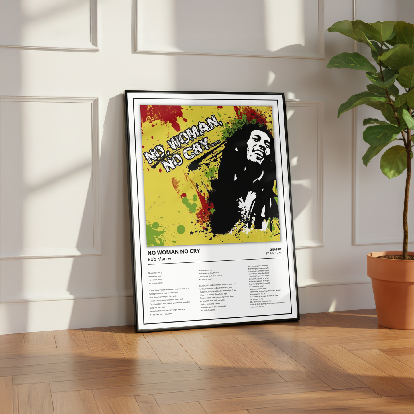 A framed Bob Marley 'No Woman No Cry' poster leaning against a white paneled wall on a wooden floor, next to a potted green plant.