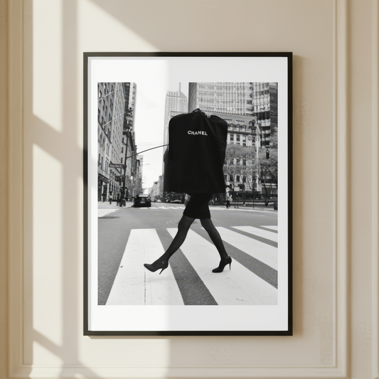 Framed black and white photo of a person crossing a street in an urban setting carrying a Chanel Clothes Bag