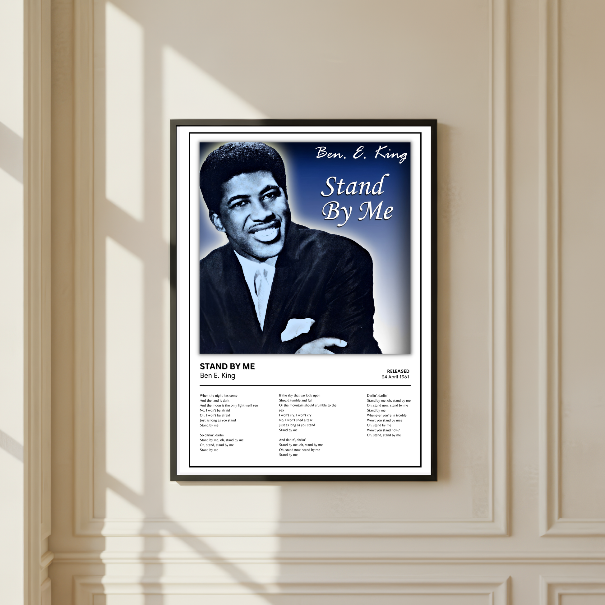 A framed Ben E. King 'Stand By Me' poster hanging on a beige paneled wall with soft window shadows.