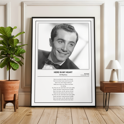 A framed black-and-white portrait print of Al Martino with the song text 'Here in My Heart' below, displayed leaning against a wall in a styled room with a plant, wood floor, and side table.