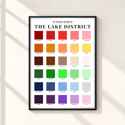 Lake District colour chart print in a thin black portrait frame on an ivory wall, featuring 30 colourful squares labelled with Cumbrian places, wildlife and food.