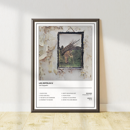 A framed wall art print leaning against a white wall on a light wood floor. The print features Led Zeppelin IV album artwork with track list text at the bottom and a dark frame around the artwork.