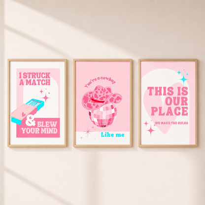 Three framed pink western-themed art prints hanging on a light beige wall. The prints feature playful text and illustrations including a match, a cowboy hat in a drink, and a heart with the phrase 'THIS IS OUR PLACE'.