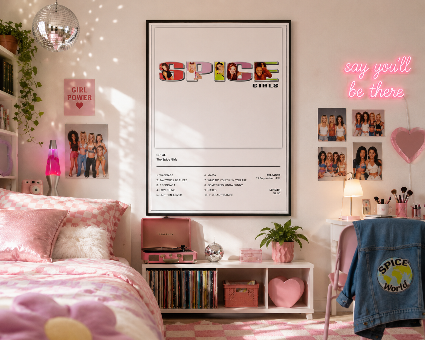 A framed Spice Girls 'Spice' music poster displayed on a wall in a styled bedroom setting. The room features pink bedding, a white shelf with pink accessories, a neon sign reading 'say you'll be there', and a denim jacket hanging on a chair.