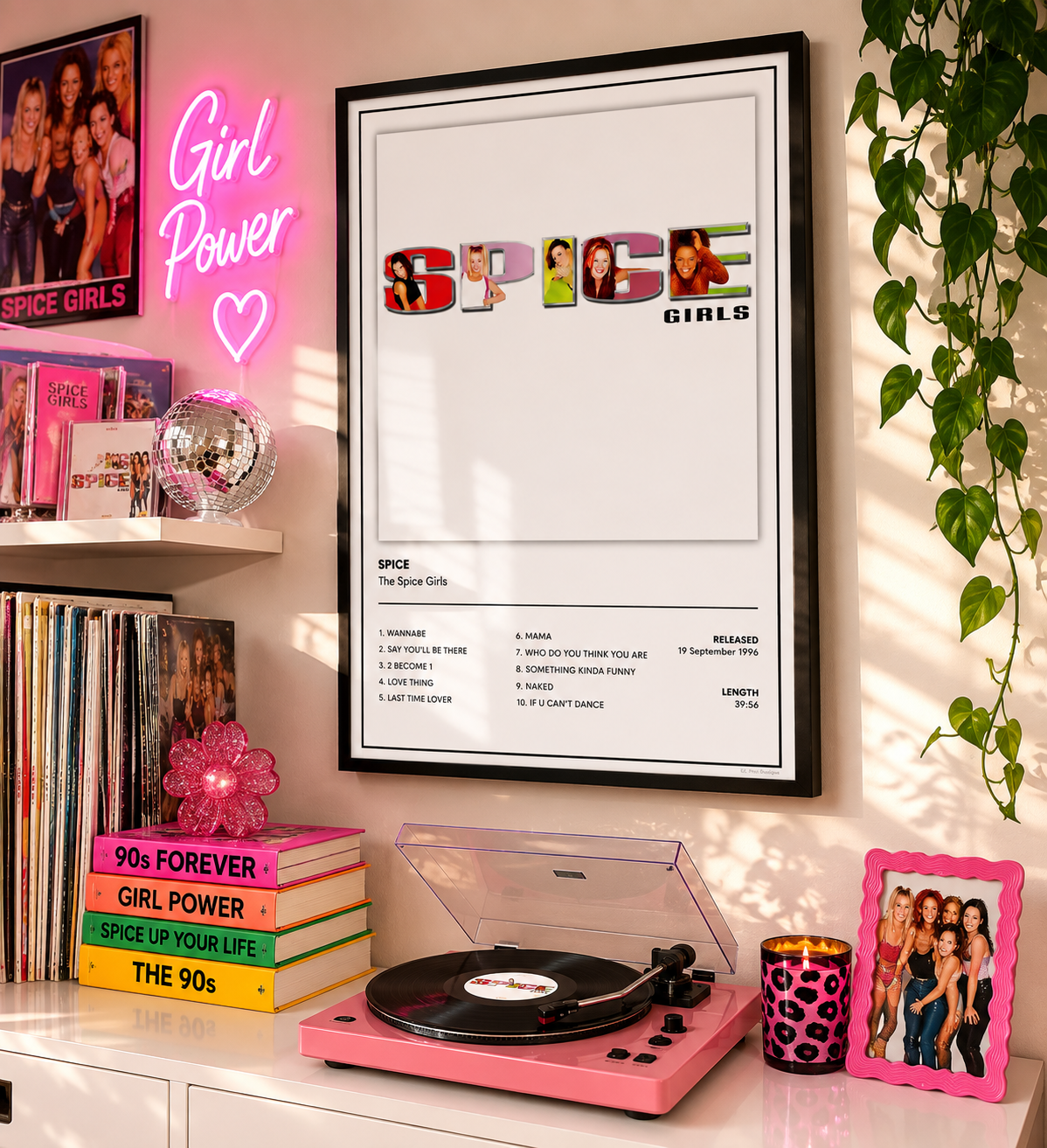 A framed Spice Girls 'Spice' wall print hangs on a wall in a styled room with a pink record player, neon sign, books, and a plant.