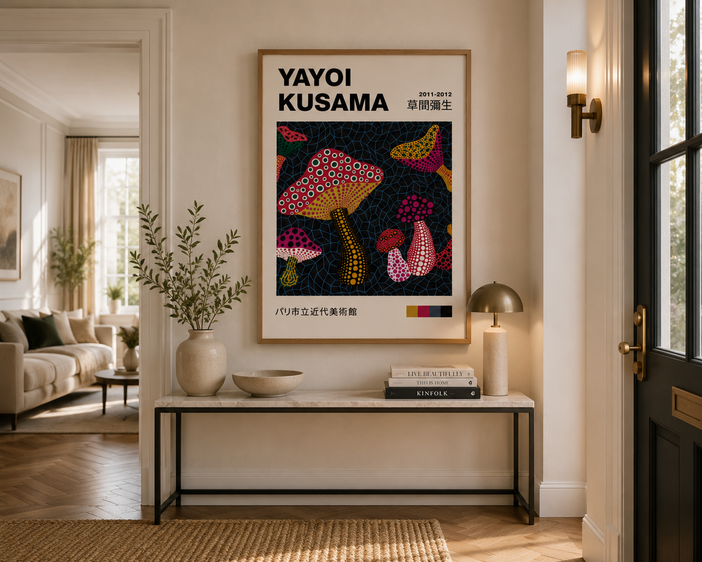 A framed art print of Yayoi Kusama's mushroom artwork hangs on a beige wall in a beautifully styled modern living room entryway with a console table, lamp, and vase.