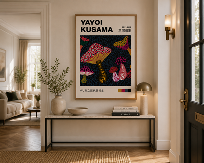 A framed art print of Yayoi Kusama's mushroom artwork hangs on a beige wall in a beautifully styled modern living room entryway with a console table, lamp, and vase.