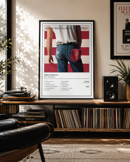 A framed music poster for Bruce Springsteen's 'Born in the USA' hangs on a wall in a styled living room with a record shelf, speakers, and plants.