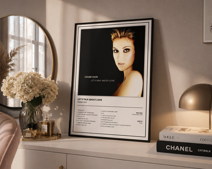 A framed music poster of Celine Dion's 'Let's Talk About Love' displayed on a white dresser in a styled room setting next to a mirror, flowers, and a Chanel book.