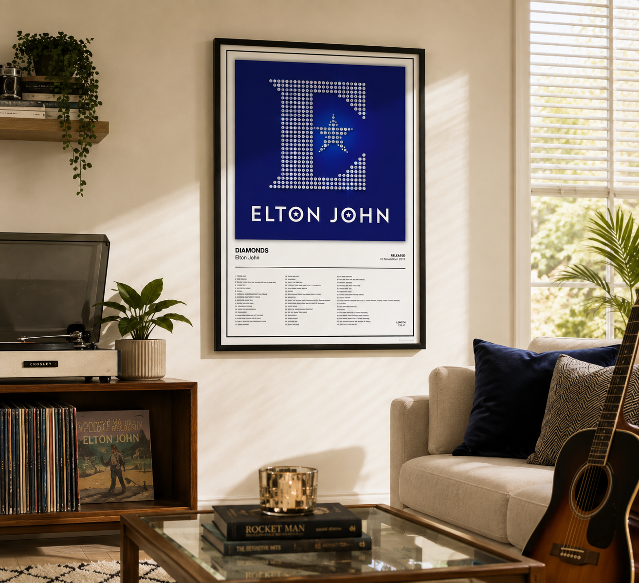 A framed Elton John 'Diamonds' wall poster hangs on a beige wall in a styled living room setting with a sofa, guitar, and record player visible.