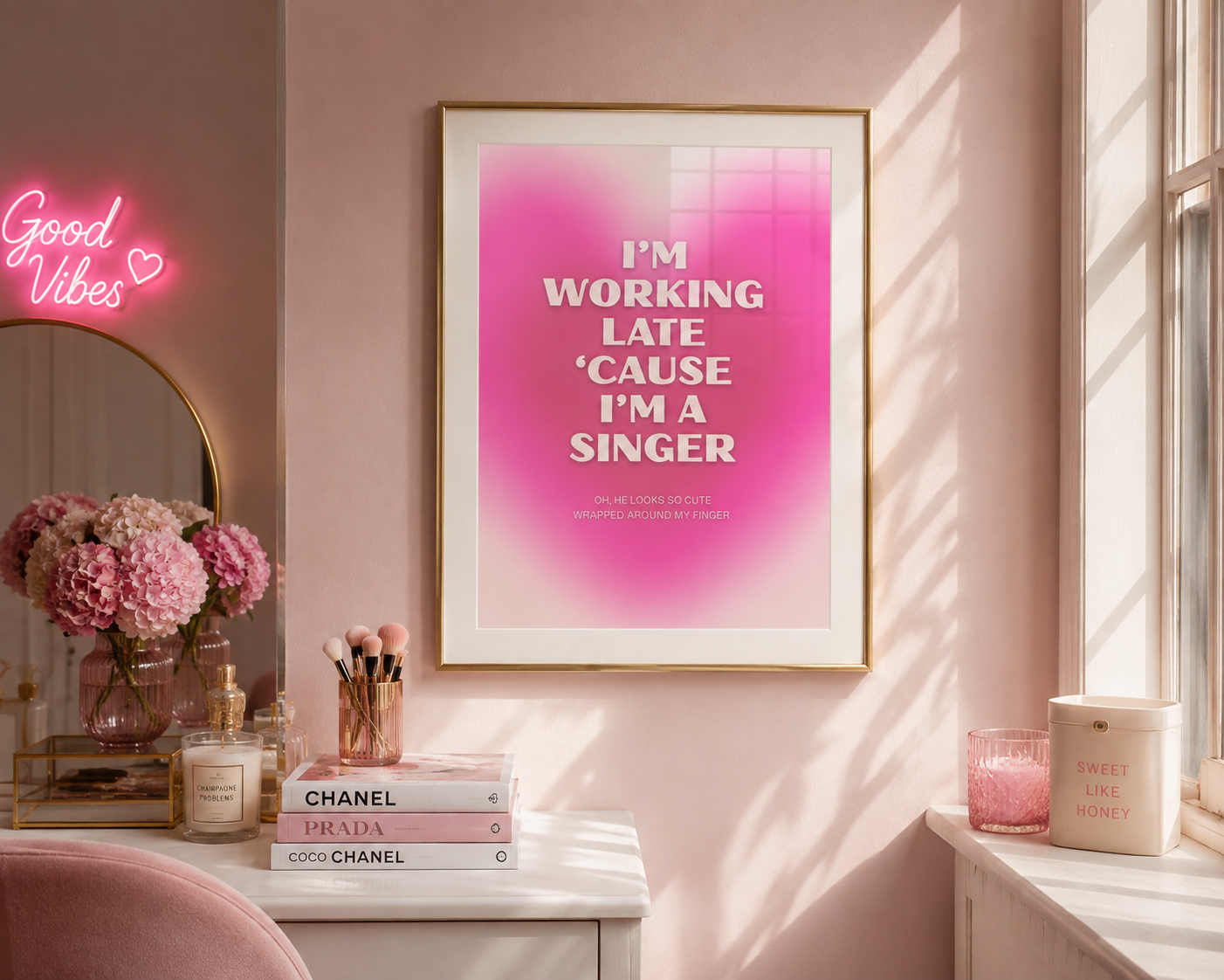 A framed art print with a pink gradient background and the text 'I'M WORKING LATE 'CAUSE I'M A SINGER' hangs on a pink wall in a styled room. The scene includes a pink neon sign, a mirror, flowers, candles, and a window with warm sunlight.