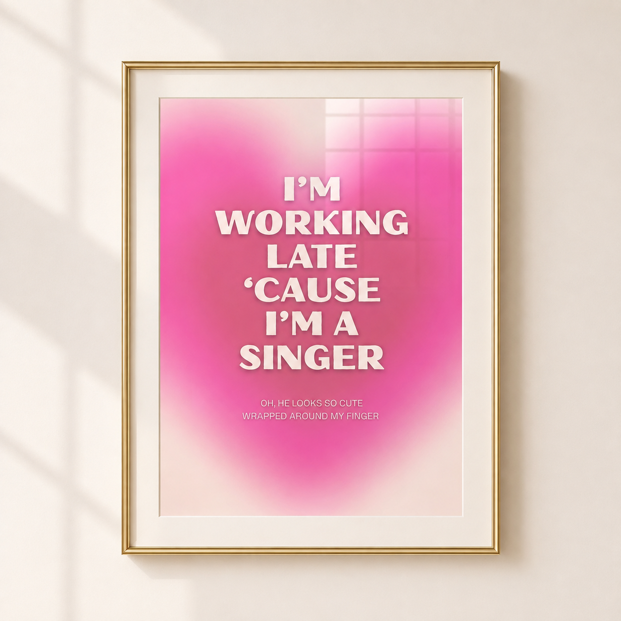 A framed typographic wall art print with a pink gradient background and white text reading, 'I'M WORKING LATE 'CAUSE I'M A SINGER,' shown hanging on a light beige wall with soft window shadows.