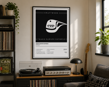 A framed black and white transit-style poster featuring the Trans Europe Express train design hangs on a wall in a styled living room with a record shelf, turntable, lamp, guitar, and sofa.
