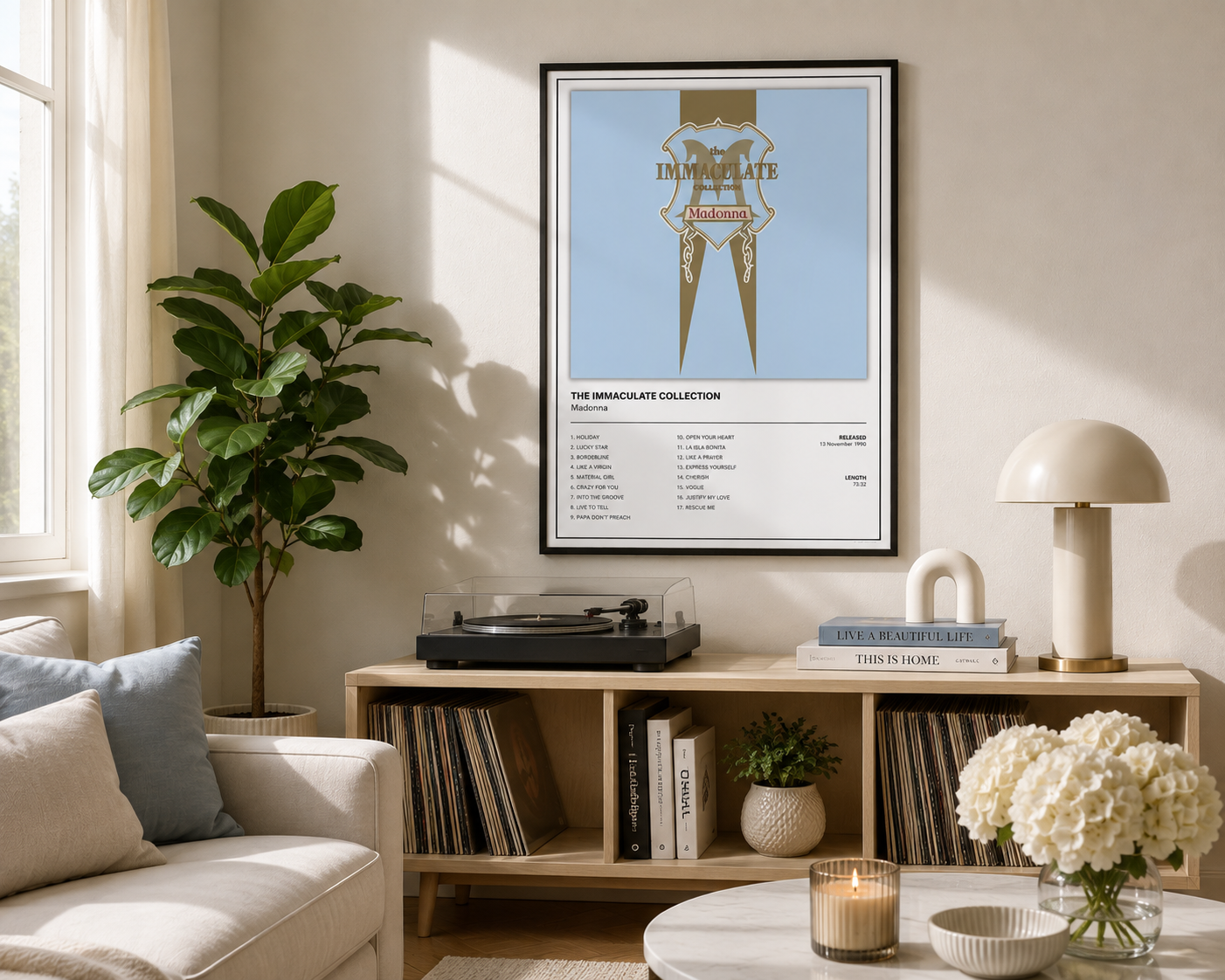 A framed wall art print featuring a minimalist graphic design with the text 'Madonna The Immaculate Collection' hangs above a wooden console table in a bright, modern living room.