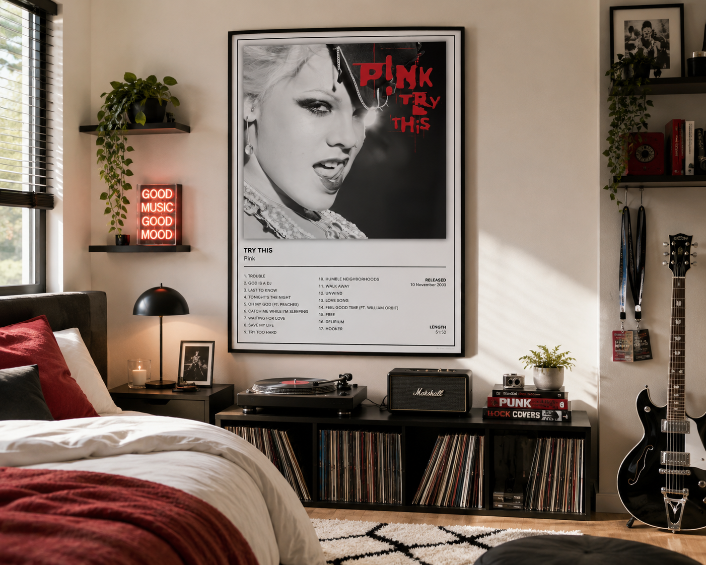 A framed 'Try This' Pink poster hangs on a wall in a styled bedroom setting with a bed, shelves, a guitar, and record players.