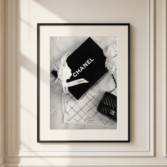 Luxury Chanel-inspired fashion wall art featuring a monochrome flat lay with a designer gift box, camellia flower and quilted handbag.