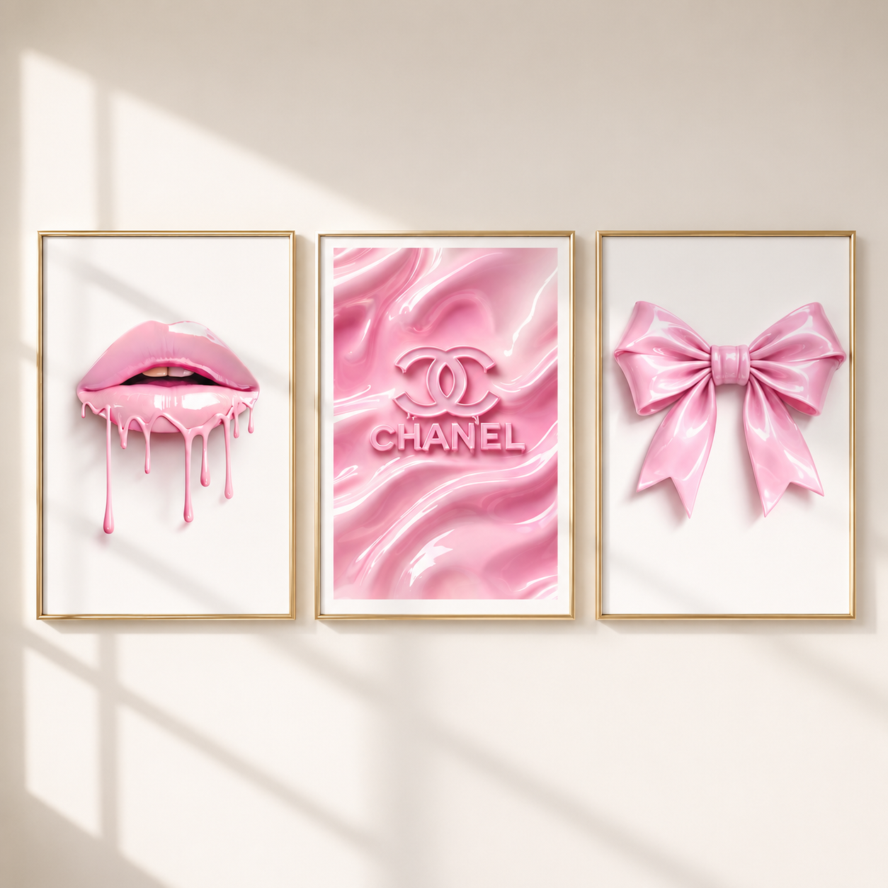 Three framed pink art prints hanging on a wall: dripping pink lips, a pink Chanel logo on a glossy pink background, and a pink satin bow. The frames are gold and the wall is light beige with soft window-shadow lighting.