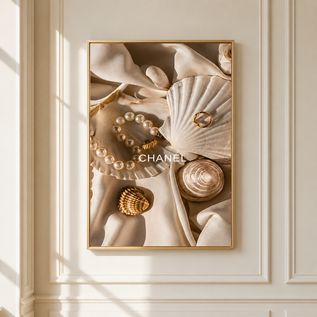 A framed wall art print featuring a luxury flat lay with a pearl bracelet, gold rings, a seashell, and draped cream fabric, displayed on a cream paneled wall with soft window shadows.