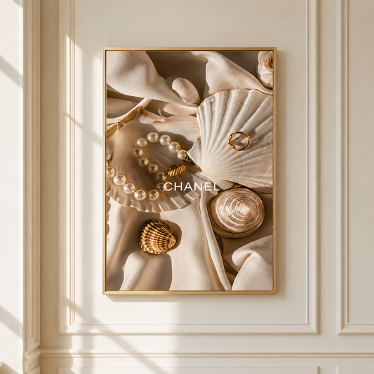 A framed wall art print featuring a luxury flat lay with a pearl bracelet, gold rings, a seashell, and draped cream fabric, displayed on a cream paneled wall with soft window shadows.