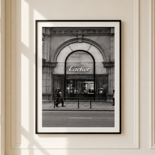 A framed black and white photograph of a Cartier storefront hanging on a cream-colored paneled wall.