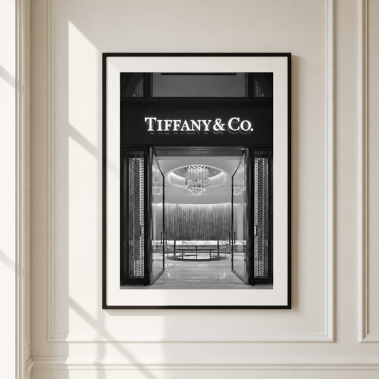 A framed black and white art print of a Tiffany & Co. storefront, mounted on a cream-colored wall with soft window shadows.