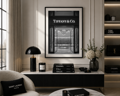 A framed black and white art print of Tiffany & Co. hanging on a beige wall in a luxury living room setting, styled with Chanel, Saint Laurent, and Tom Ford products.