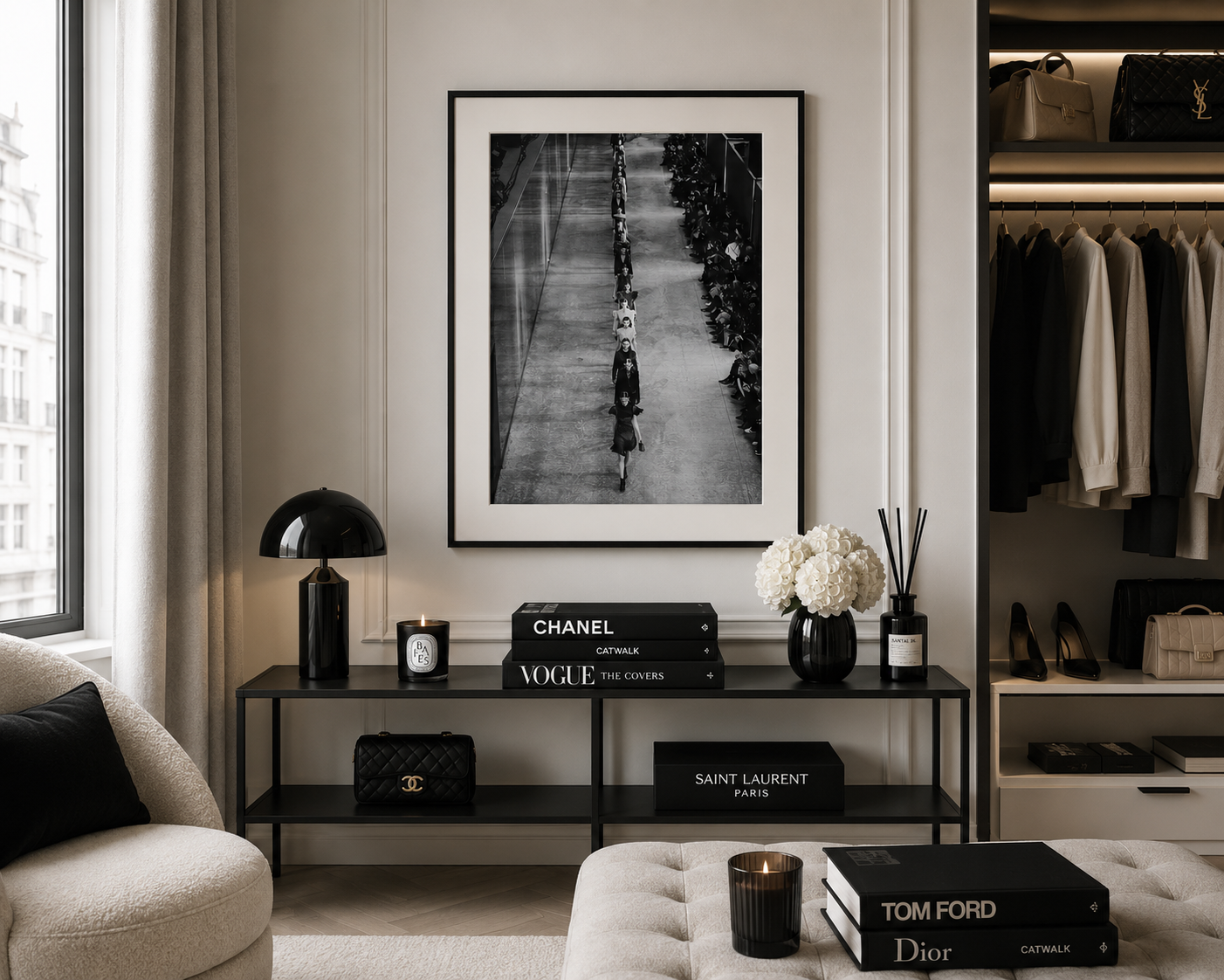 A black and white framed art print hangs on a beige wall in a styled room setting above a black console table with decorative items including Chanel, Vogue, and Saint Laurent boxes.