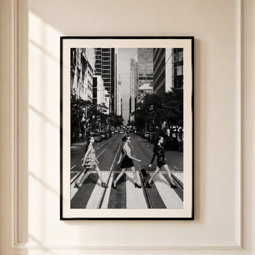 A framed black and white art print of the iconic Abbey Road crosswalk scene, displayed on a cream-colored wall with decorative molding and soft window shadows.