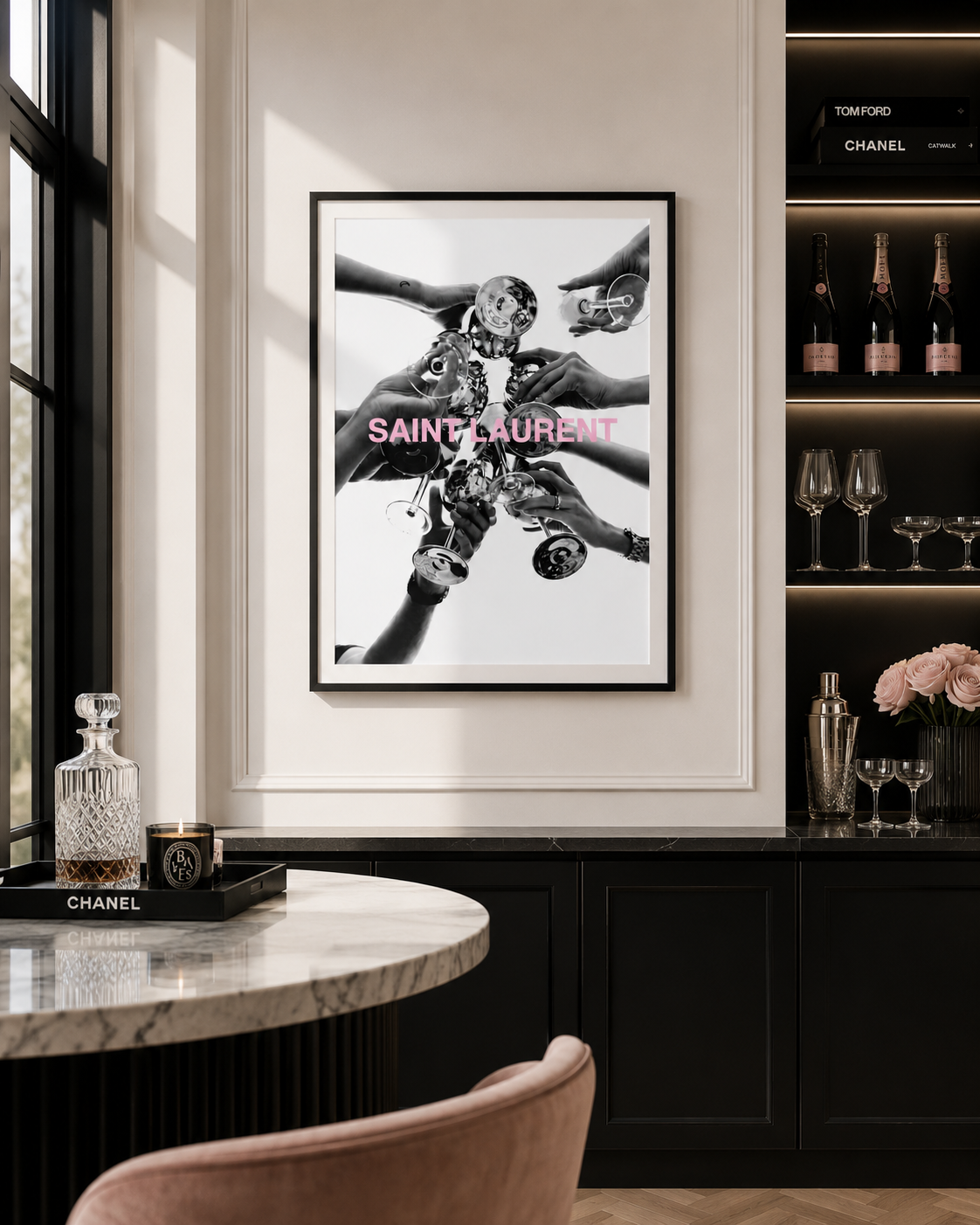 A framed black and white Saint Laurent art print with pink lettering, displayed on a white wall in a luxury interior setting with a marble table and dark wood cabinetry.