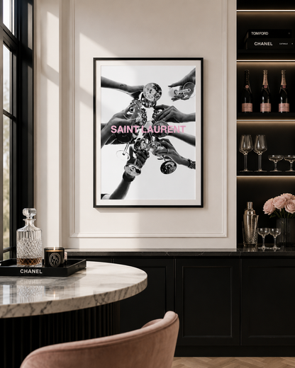A framed black and white Saint Laurent art print with pink lettering, displayed on a white wall in a luxury interior setting with a marble table and dark wood cabinetry.