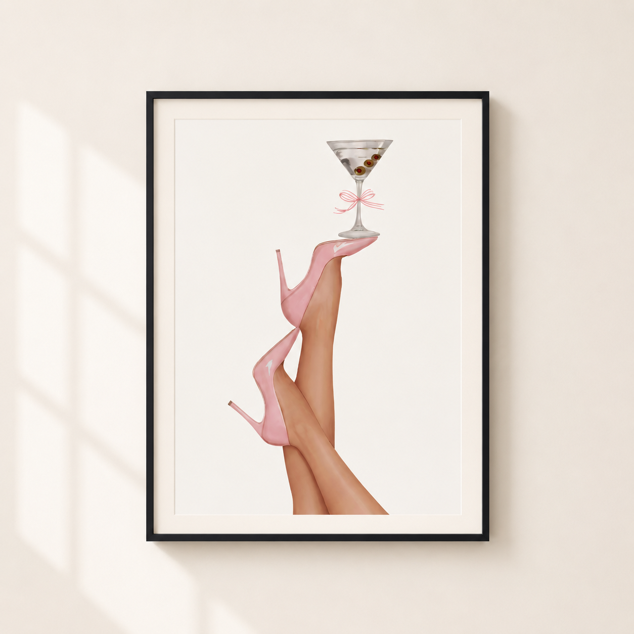 Framed wall art print featuring a stylized illustration of legs wearing pink high heels balancing a martini glass, displayed on a light beige wall with soft window-shadow lighting.