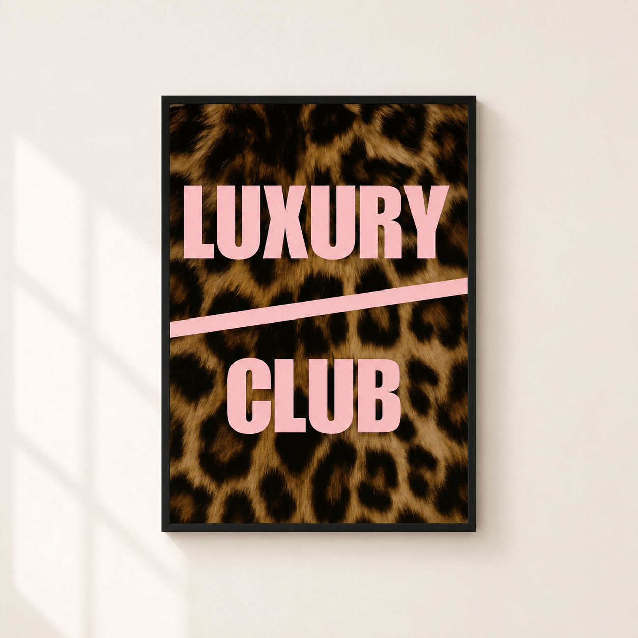 A framed poster with a leopard print background and the words 'LUXURY CLUB' in pink lettering, hanging on a light beige wall with soft window shadows.
