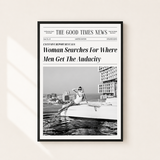 A framed black-and-white newspaper-style poster hanging on a light beige wall. The poster mimics a newspaper front page with the headline 'Woman Searches For Where Men Get The Audacity' and a black-and-white photo of a woman sitting on a boat.
