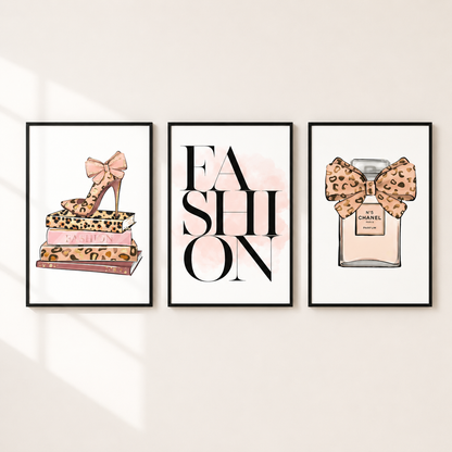 Three framed fashion-themed wall art prints displayed on a light beige wall. The left print shows a leopard-print high heel resting on stacked fashion books; the center print features the word 'FASHION' in large black letters with a soft pink watercolor splash; the right print shows a perfume bottle with a leopard-print bow and a small Chanel label.