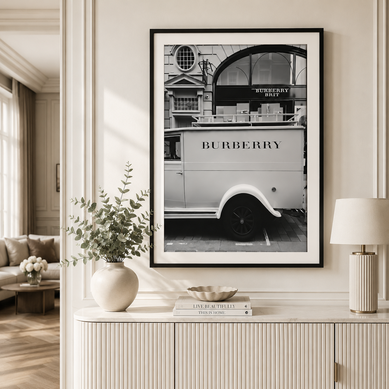 A framed black and white art print of a vintage Burberry truck displayed on a cream-colored wall above a console table with decorative items.