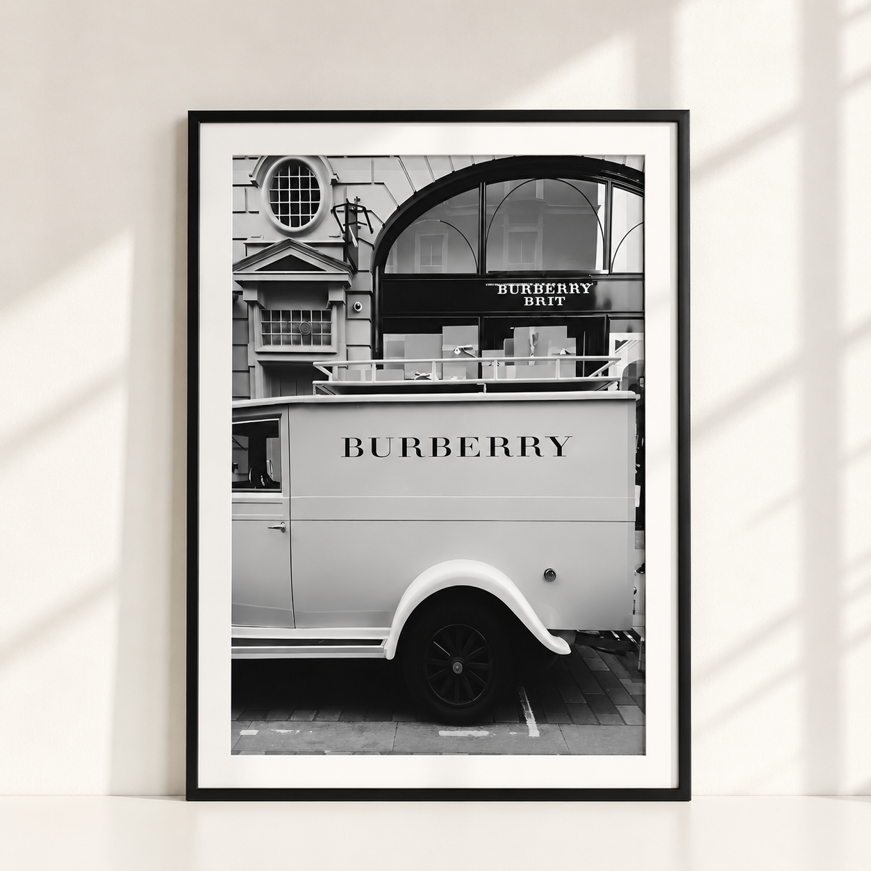 A framed black and white art print leaning against a white wall, featuring a vintage Burberry delivery van in front of a building with a Burberry Duffel sign.
