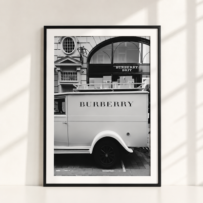 A framed black and white art print leaning against a white wall, featuring a vintage Burberry delivery van in front of a building with a Burberry Duffel sign.