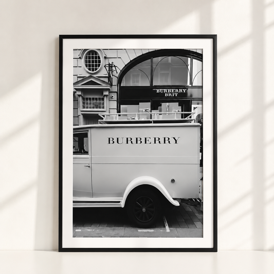 A framed black and white art print leaning against a white wall, featuring a vintage Burberry delivery van in front of a building with a Burberry Duffel sign.