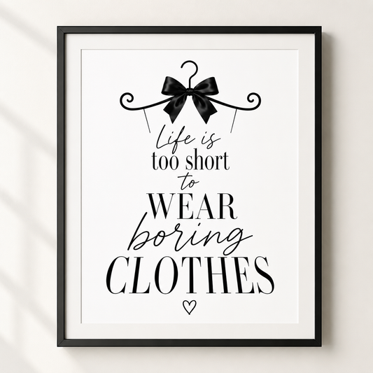 A framed typographic wall art print with the quote 'Life is too short to WEAR boring CLOTHES' in black text on a white background, with a black hanger and bow illustration at the top. The frame is black and mounted against a light neutral wall.