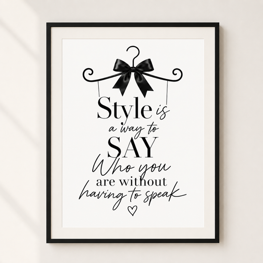 A framed typographic wall art print with a black hanger and bow illustration at the top and the quote, 'Style is a way to SAY Who you are without having to speak,' in black lettering on a white background. The frame is shown hanging against a light neutral wall.