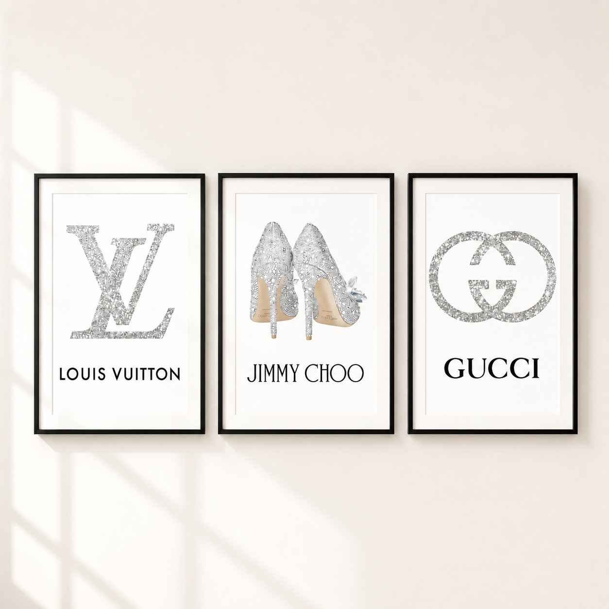 Three framed fashion art prints hanging on a light beige wall. The left print shows a silver Louis Vuitton LV logo and name.