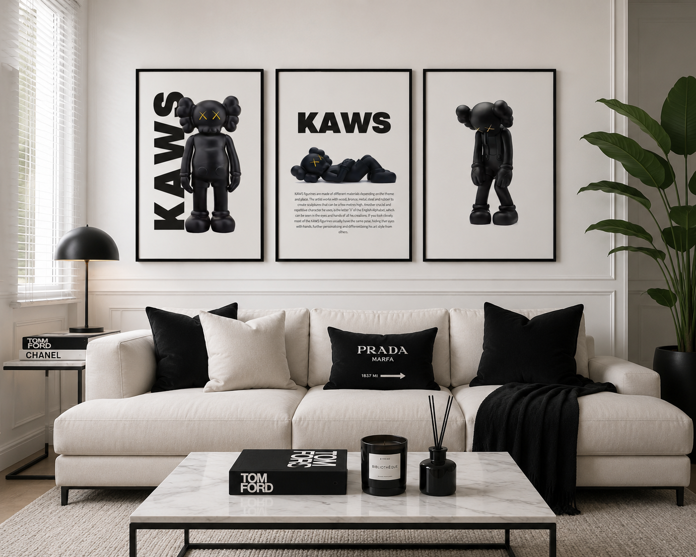 Three framed black and white 'KAWS' art prints are displayed on a white wall above a modern white sofa with black accent pillows. The room is styled with a marble coffee table, a black side table with a lamp, and a large green plant.
