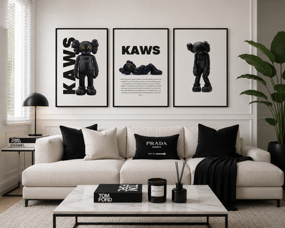 Three framed black and white 'KAWS' art prints are displayed on a white wall above a modern white sofa with black accent pillows. The room is styled with a marble coffee table, a black side table with a lamp, and a large green plant.