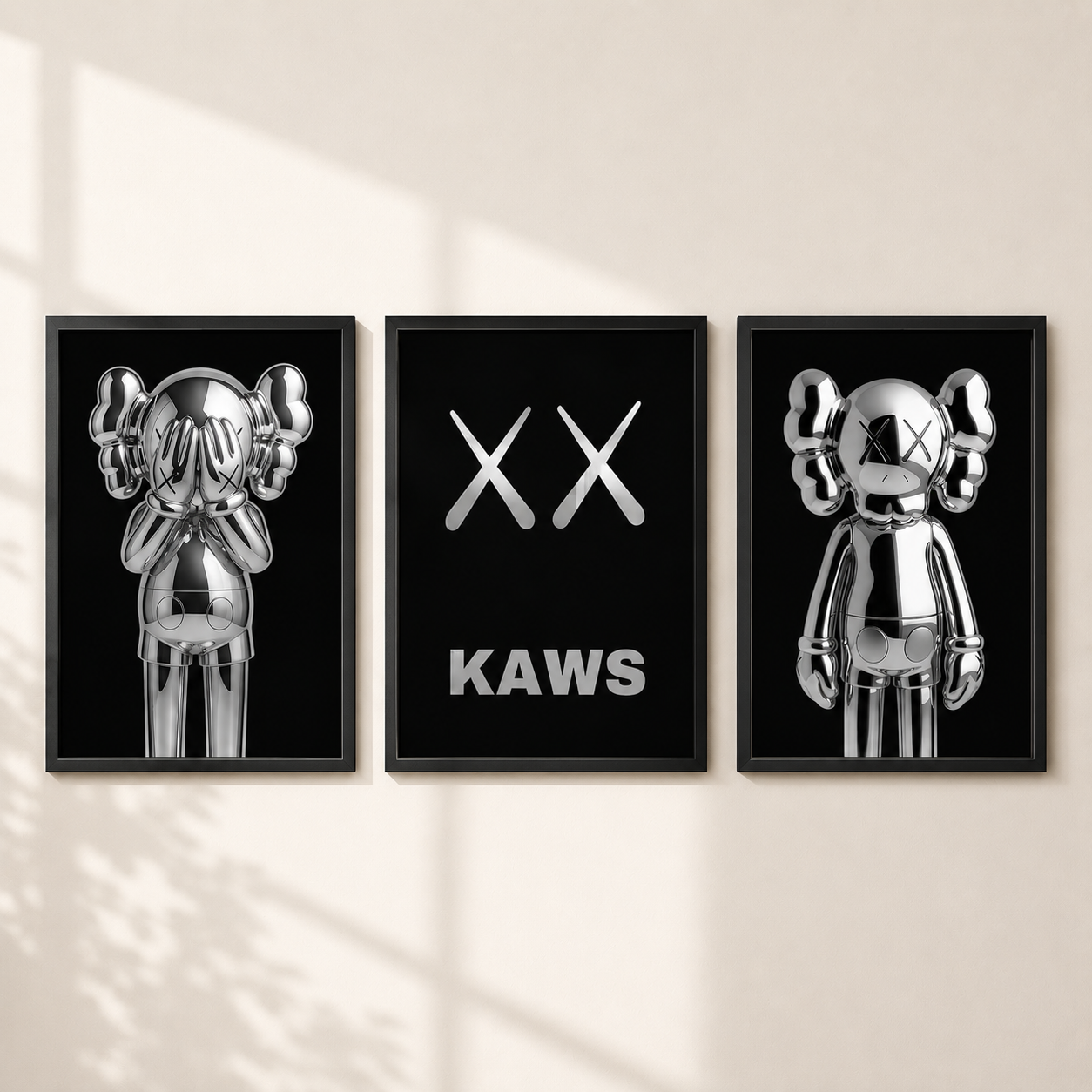 Three framed wall art prints featuring reflective silver KAWS character figures and the XX logo on black backgrounds, displayed side by side on a light beige wall with soft window shadow patterns.