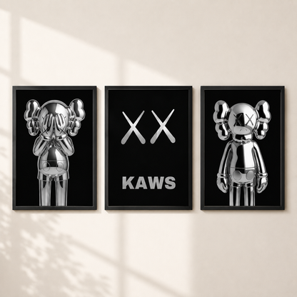 Three framed wall art prints featuring reflective silver KAWS character figures and the XX logo on black backgrounds, displayed side by side on a light beige wall with soft window shadow patterns.