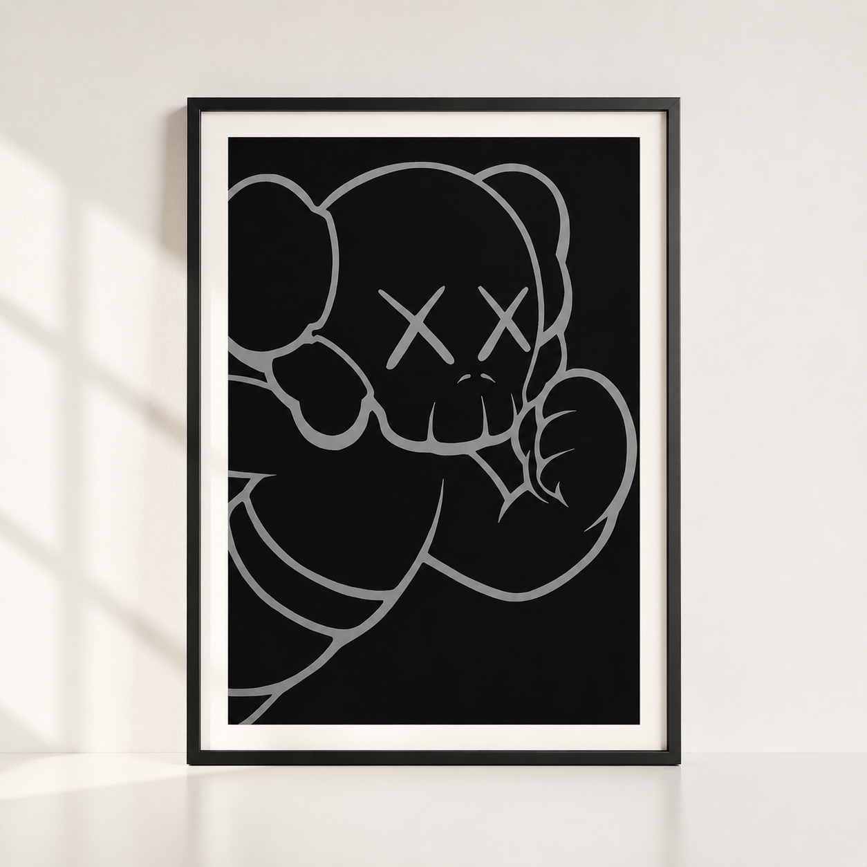 A framed art print featuring a minimalist black and white line drawing of a bear with an X for a eye, styled leaning against a white wall with soft window shadows.
