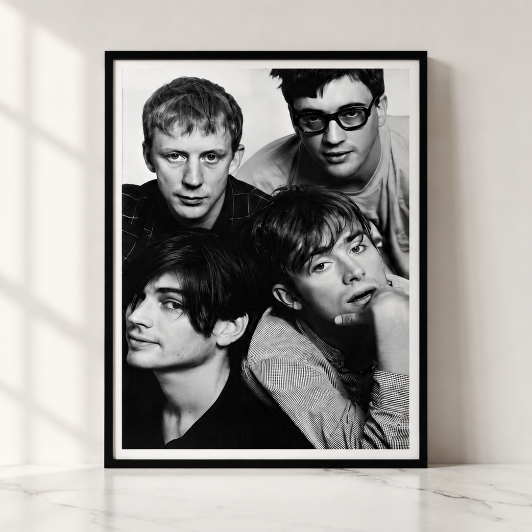A framed black and white portrait print of the band Blur leaning against a light wall on a marble surface, with soft window shadows cast across the scene.