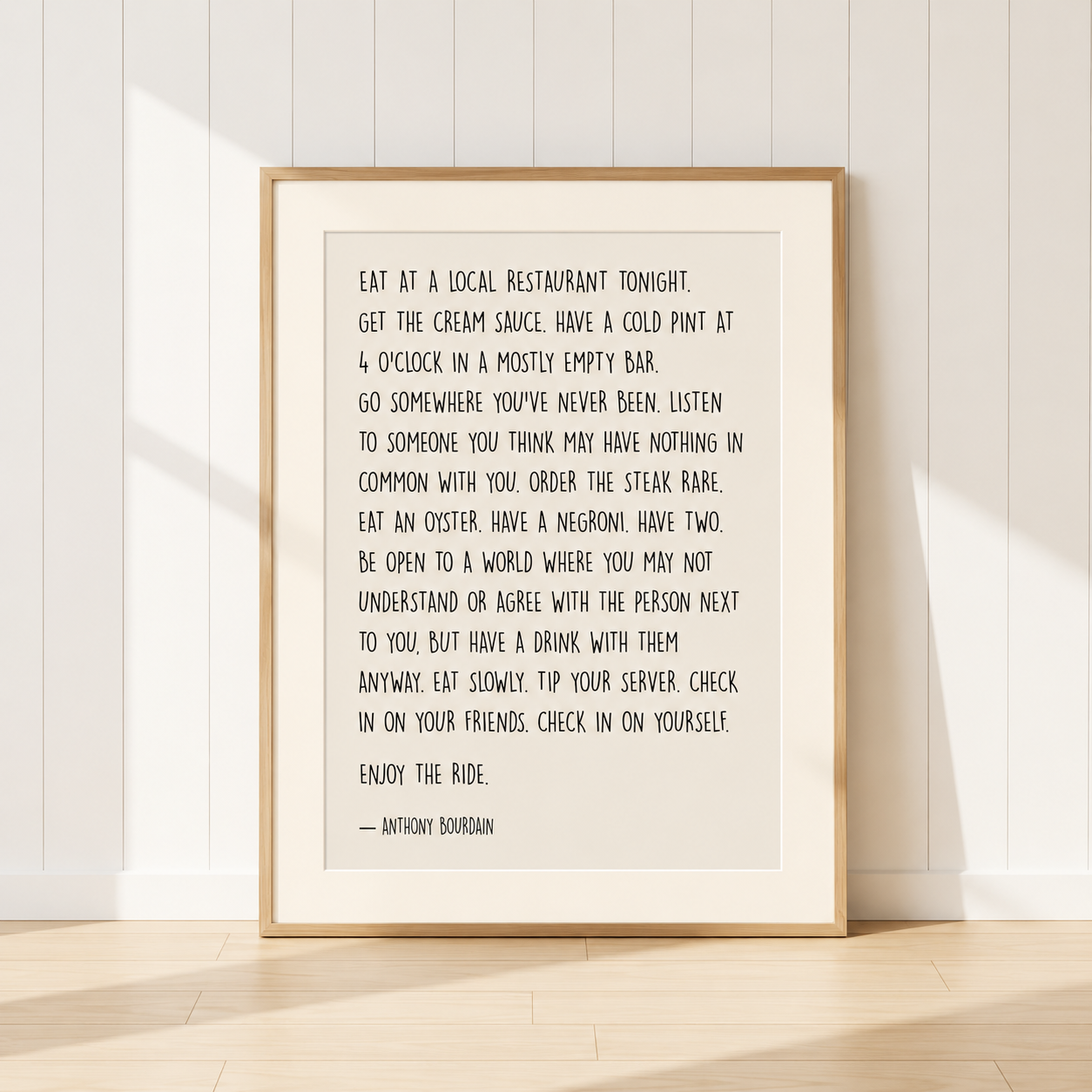 Anthony Bourdain quote typography print in light oak frame with warm ivory mount on neutral background.