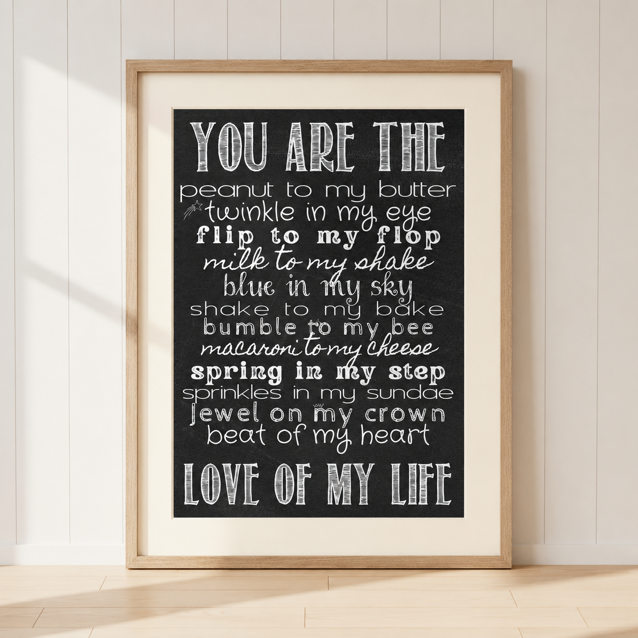 Romantic "You Are The Love Of My Life" typography print featuring sweet love sayings in white text on a black chalkboard background, displayed in a light oak frame with warm ivory mount.